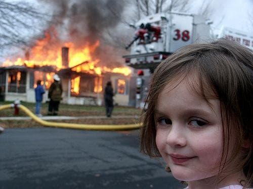 Disaster Girl smiling in front of a burning house